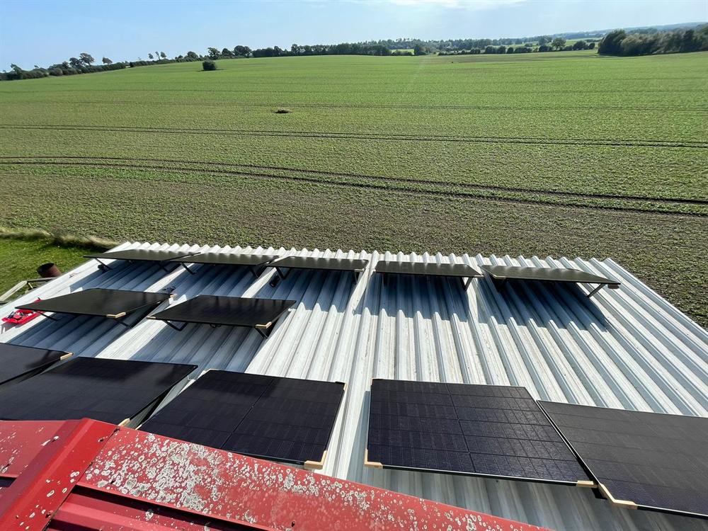 Photovoltaikmodule auf einem Wellblechdach, im Hintergrund ein Feld